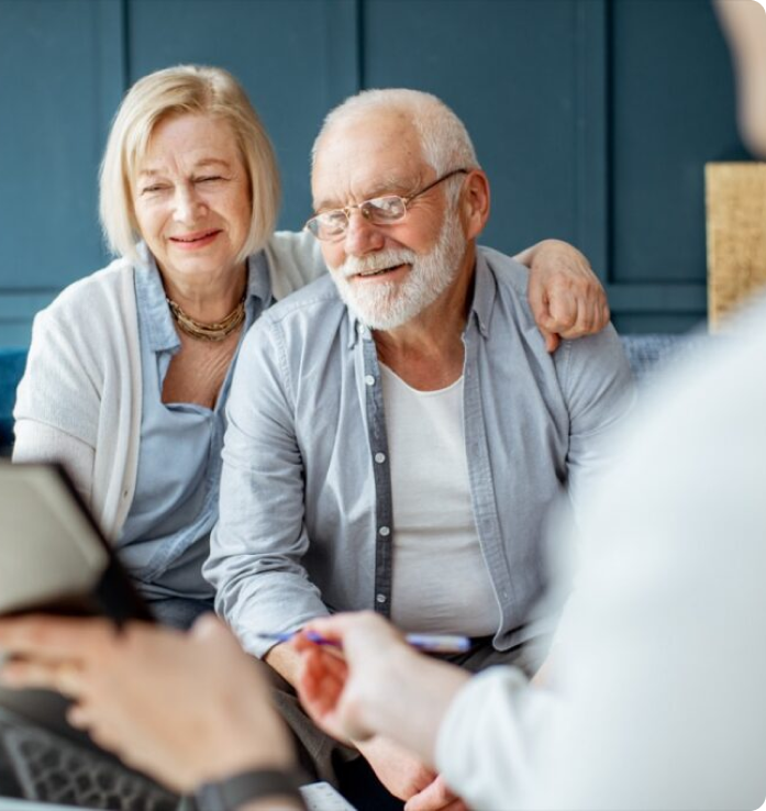 An elderly couple smiles while sitting across from a professional holding a pen and documents.