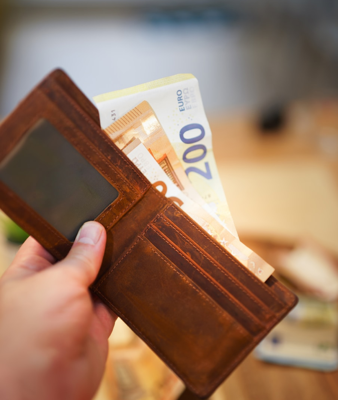 A close-up shot of a hand holding an open brown leather wallet containing several 200 Euro banknotes.