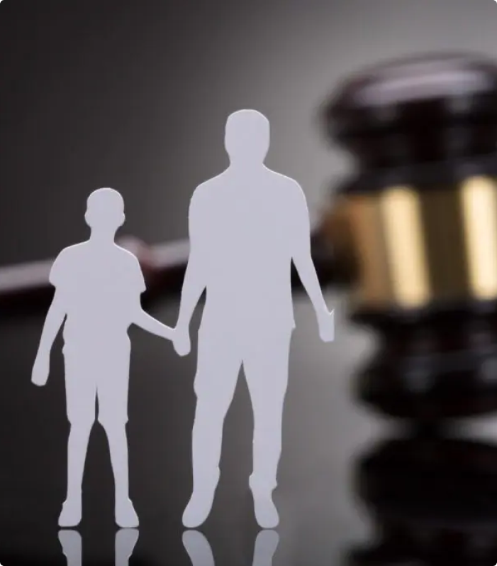 A paper cutout of a father and son stands in front of a blurred judge's gavel.